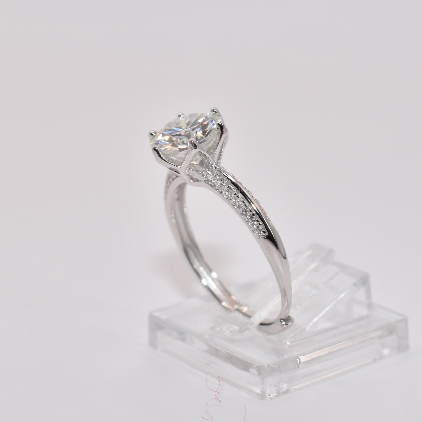 Silver ring with a 2Ct moissanite diamond on a clear stand against a light gray background