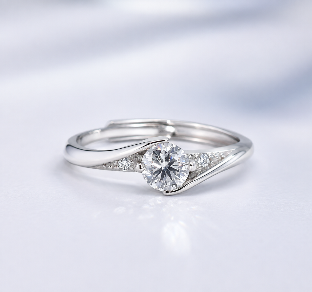 A silver-toned diamond ring with a round-cut center stone and small accent diamonds on a split shank, photographed on a soft white background.