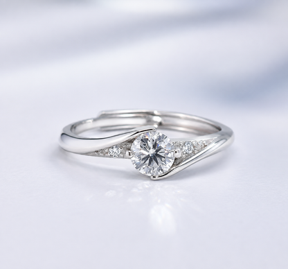 A silver-toned diamond ring with a round-cut center stone and small accent diamonds on a split shank, photographed on a soft white background.