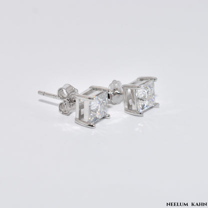 Silver stud earrings with clear 1ct Moissanite gemstones on a light gray background, branded 'Neelum Kahn'.