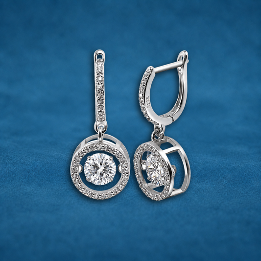 Silver earrings with circular designs and clear stones on a blue background