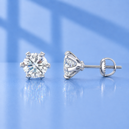 A pair of silver stud earrings with round brilliant-cut clear gemstones, shown from the front and side on a reflective light blue surface.