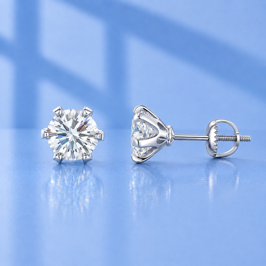 A pair of silver stud earrings with round brilliant-cut clear gemstones, shown from the front and side on a reflective light blue surface.