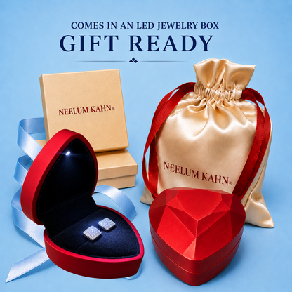 Neelum Kahn jewelry gift set packaging and accessories on a light blue background, including a red heart-shaped jewelry box, an open red heart box with earrings, a beige jewelry box, a beige satin drawstring pouch, and a faceted red heart-shaped box, with text reading 'COMES IN AN LED JEWELRY BOX GIFT READY'.